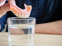 a person putting dentures in a glass of water