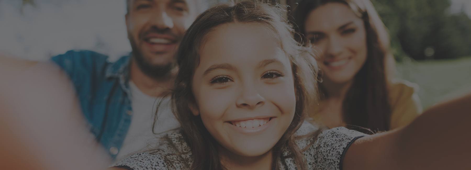 Young girl taking selfie with her parents in background
