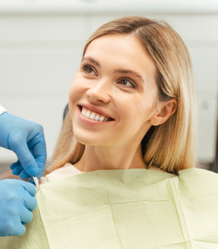 Blonde woman smiling up at dentist while they adjust cloth