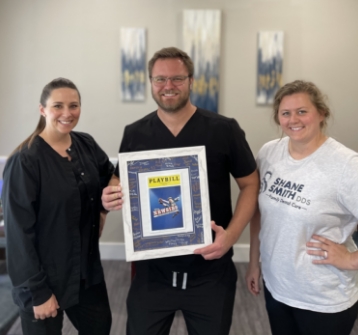 Dental team holding up a framed playbill