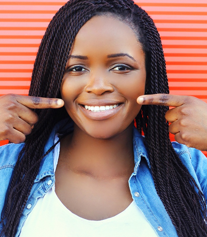 Woman pointing to smile after metal free dental restorations