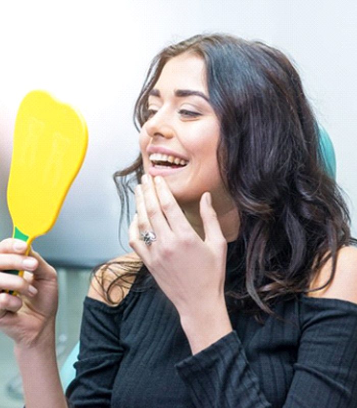 woman admiring her new dental crown in a mirror