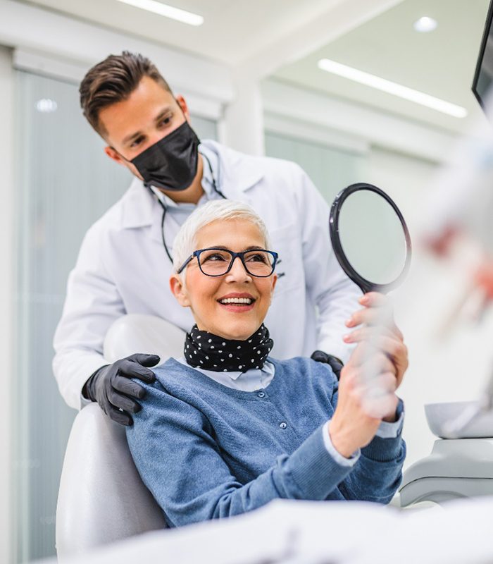 smiling dental patient holding up mirror 