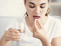 woman taking pill with glass of water 