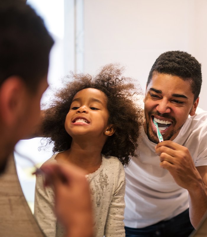 Young girl and father brushing teeth together after children's dentistry visit
