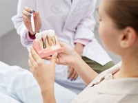 Dentist showing young woman a model of a dental implant in Jonesboro, AR