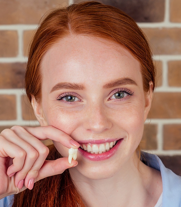 Woman holding up an extracted wisdom tooth to her smile